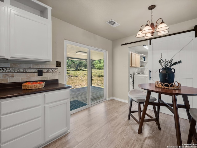 dining space with visible vents, washing machine and dryer, a barn door, baseboards, and light wood-style floors