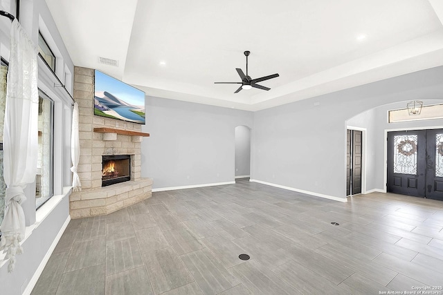 unfurnished living room with ceiling fan, visible vents, arched walkways, a fireplace, and a raised ceiling