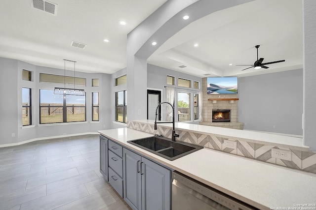 kitchen with a sink, a stone fireplace, open floor plan, stainless steel dishwasher, and visible vents