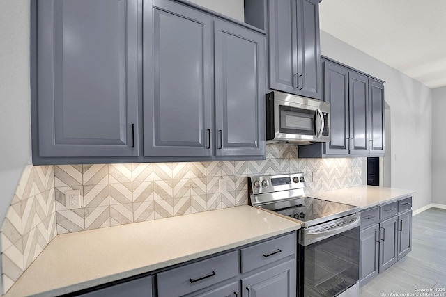 kitchen featuring gray cabinets, appliances with stainless steel finishes, tasteful backsplash, light countertops, and baseboards