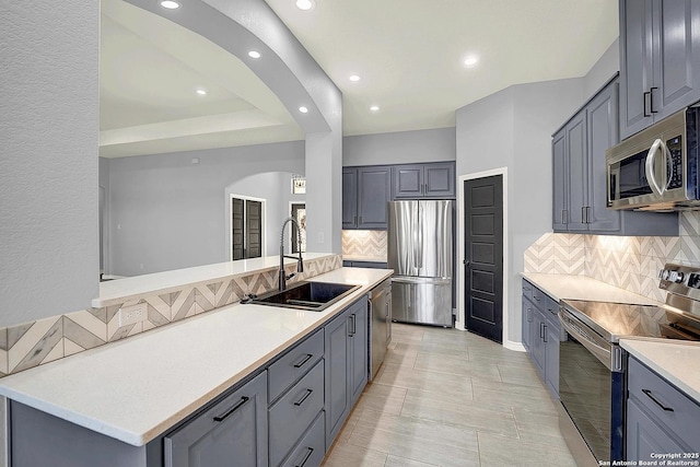 kitchen with appliances with stainless steel finishes, a sink, arched walkways, decorative backsplash, and gray cabinetry