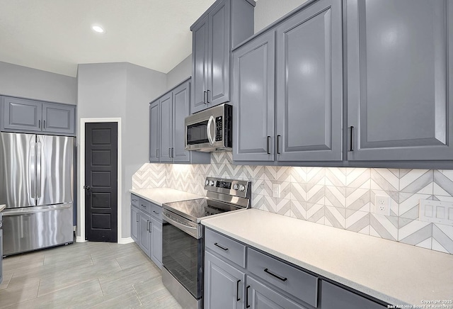 kitchen with decorative backsplash, baseboards, light countertops, gray cabinetry, and stainless steel appliances