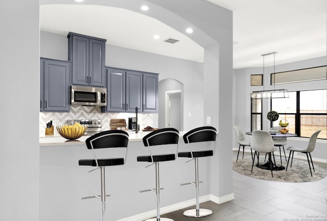 kitchen featuring a kitchen breakfast bar, light countertops, stainless steel microwave, tasteful backsplash, and arched walkways