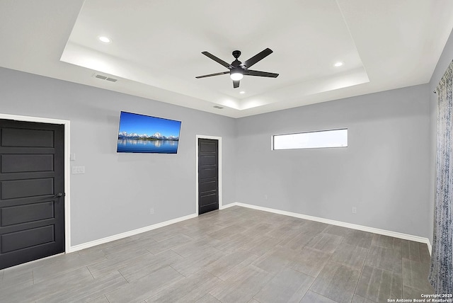 empty room featuring a raised ceiling, a ceiling fan, baseboards, recessed lighting, and visible vents