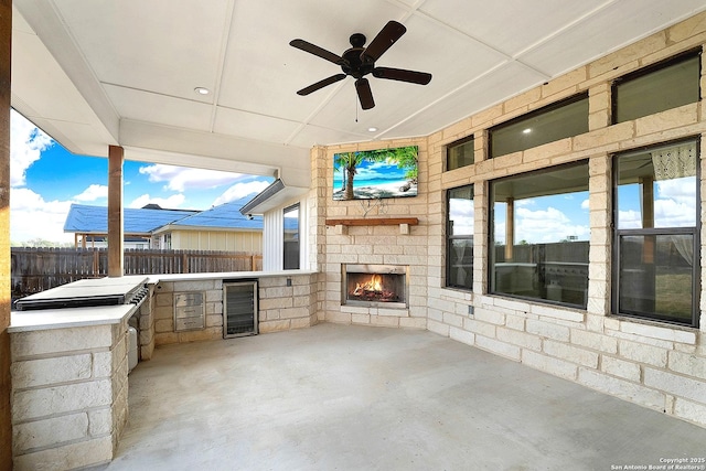 view of patio / terrace with fence, beverage cooler, a large fireplace, a ceiling fan, and exterior kitchen