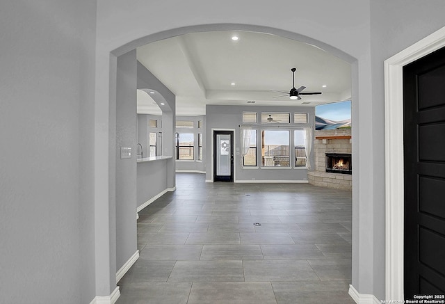 foyer featuring a ceiling fan, a stone fireplace, arched walkways, baseboards, and recessed lighting