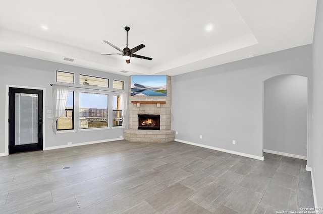 unfurnished living room featuring visible vents, arched walkways, ceiling fan, and a tray ceiling