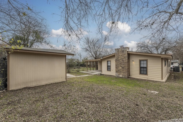 back of property with fence, an outdoor structure, a chimney, and cooling unit