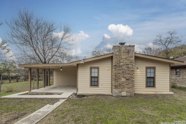 rear view of house with fence, a patio, a chimney, an attached carport, and a yard