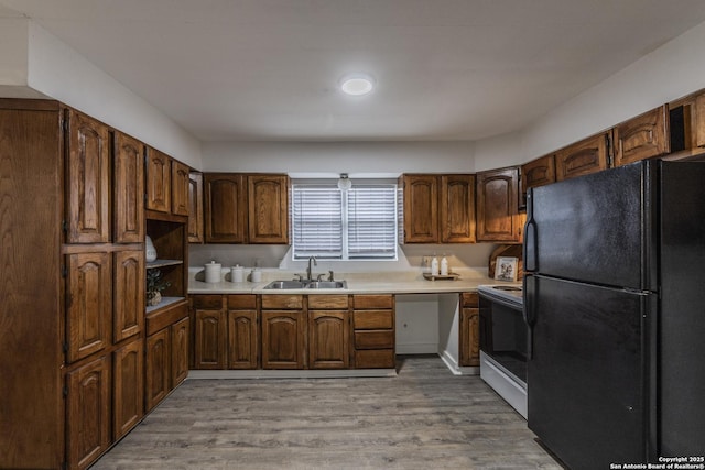 kitchen featuring freestanding refrigerator, range with electric stovetop, light countertops, a sink, and light wood finished floors