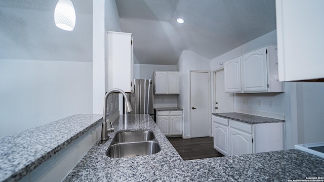 kitchen featuring freestanding refrigerator, lofted ceiling, dark stone counters, white cabinetry, and a sink