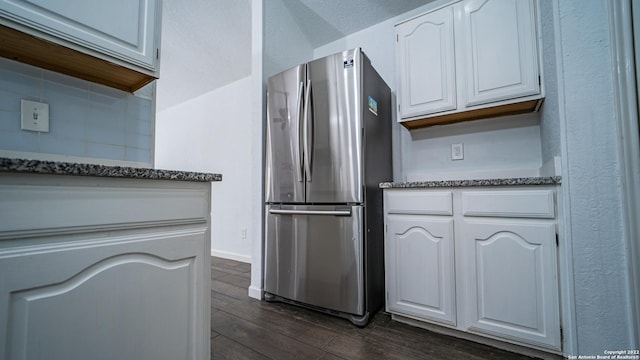 kitchen with white cabinets, freestanding refrigerator, dark stone counters, baseboards, and dark wood-type flooring