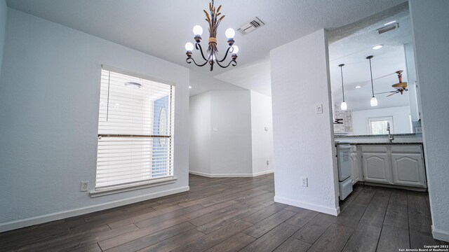 unfurnished dining area featuring visible vents, dark wood-style flooring, ceiling fan with notable chandelier, and baseboards