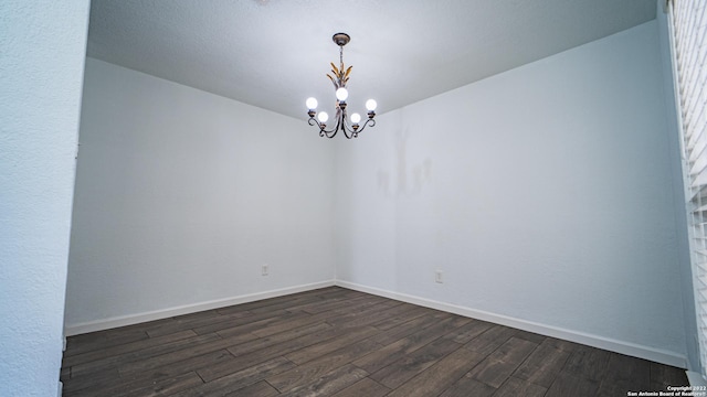 unfurnished room featuring baseboards, a chandelier, and dark wood-style floors