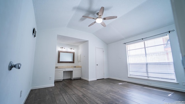 unfurnished bedroom featuring built in desk, ensuite bath, baseboards, lofted ceiling, and dark wood-style floors