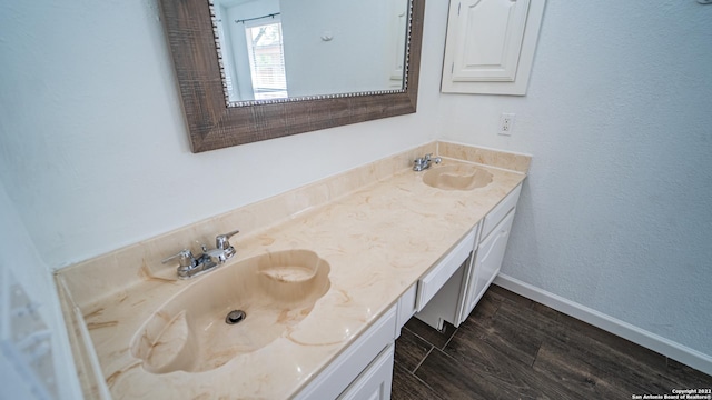 full bathroom with double vanity, baseboards, a sink, and wood finished floors