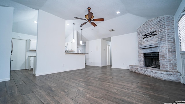 unfurnished living room featuring ceiling fan, a fireplace, vaulted ceiling, and dark wood-style floors