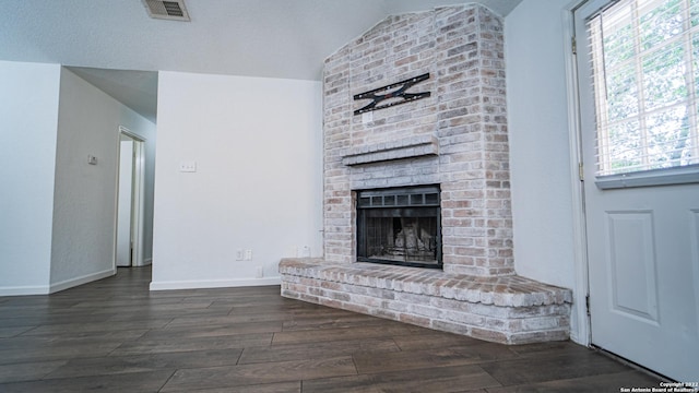 unfurnished living room with plenty of natural light, a brick fireplace, wood finished floors, and visible vents