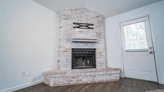 interior space featuring a textured wall, a fireplace, dark wood finished floors, baseboards, and lofted ceiling