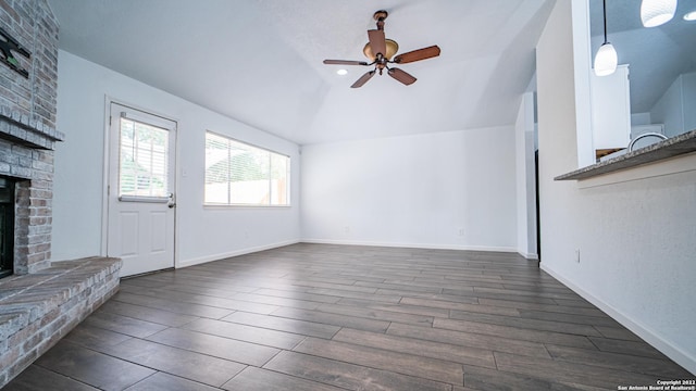 unfurnished living room featuring dark wood-style flooring, lofted ceiling, a fireplace, baseboards, and ceiling fan