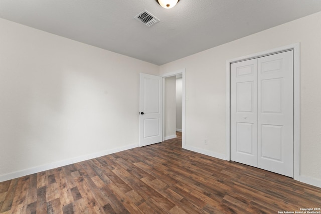 unfurnished bedroom featuring baseboards, visible vents, dark wood finished floors, and a closet