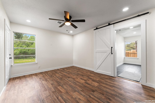 empty room featuring visible vents, wood finished floors, baseboards, ceiling fan, and a barn door