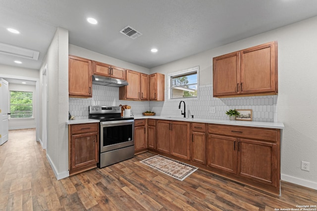 kitchen featuring visible vents, stainless steel range with electric stovetop, light countertops, under cabinet range hood, and a sink