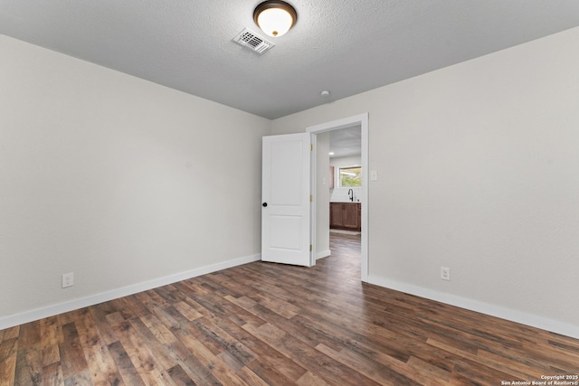 empty room featuring visible vents, baseboards, and dark wood-style flooring