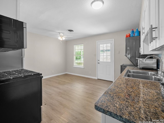 kitchen with a ceiling fan, dark countertops, light wood-style floors, baseboards, and a sink