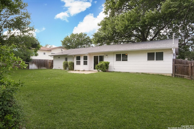 rear view of property featuring roof with shingles, a yard, and fence private yard