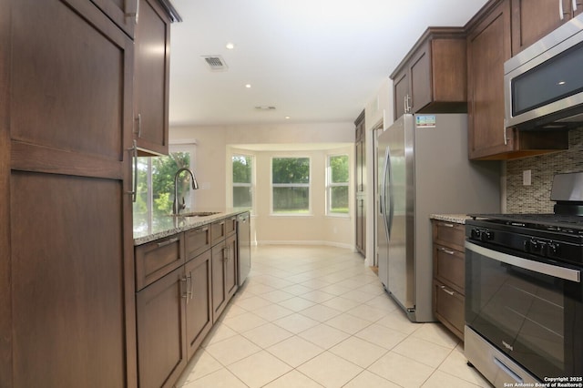 kitchen featuring dark brown cabinetry, tasteful backsplash, light stone counters, a sink, and appliances with stainless steel finishes