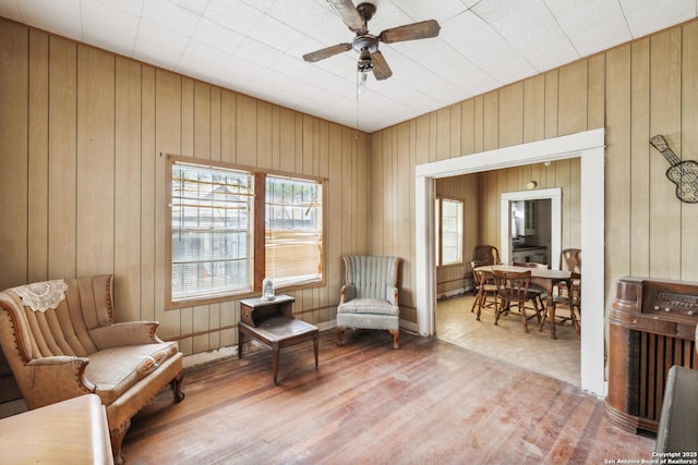 sitting room with wood walls, ceiling fan, and wood finished floors
