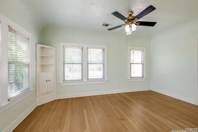 spare room with baseboards, a ceiling fan, light wood-type flooring, and visible vents