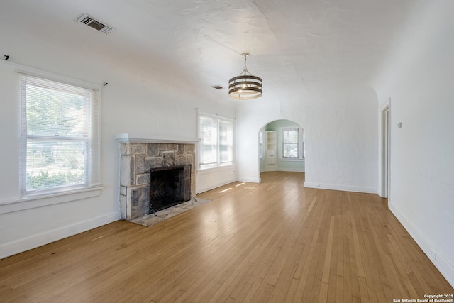 unfurnished living room with visible vents, wood finished floors, a fireplace, baseboards, and arched walkways