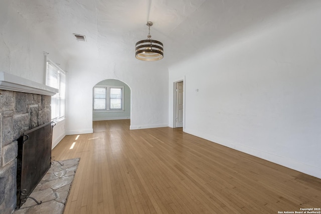 unfurnished living room featuring visible vents, baseboards, a chandelier, arched walkways, and light wood-style flooring