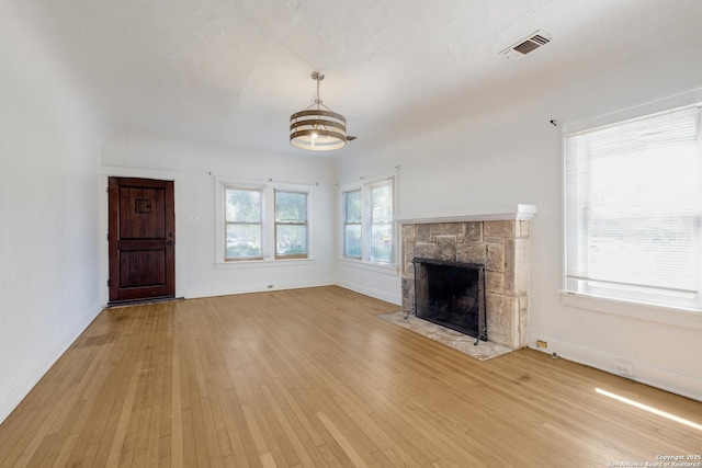 unfurnished living room featuring light wood finished floors, a fireplace, a chandelier, baseboards, and visible vents