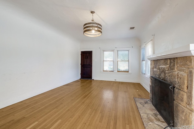 unfurnished living room featuring an inviting chandelier, a stone fireplace, light wood-style flooring, baseboards, and visible vents