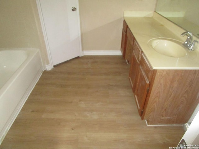 bathroom featuring vanity, baseboards, a bathing tub, and wood finished floors