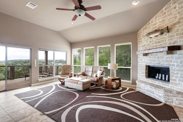 living room with tile patterned flooring, visible vents, a stone fireplace, a ceiling fan, and vaulted ceiling