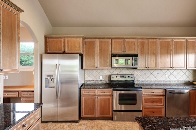kitchen with dark stone counters, stainless steel appliances, arched walkways, and backsplash