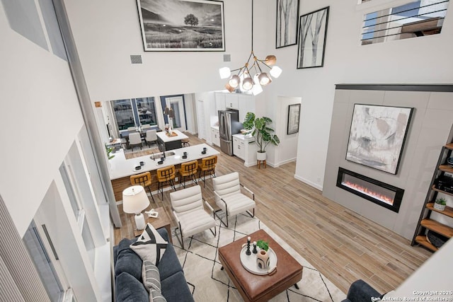 living room featuring visible vents, an inviting chandelier, light wood-style floors, a high ceiling, and a tile fireplace