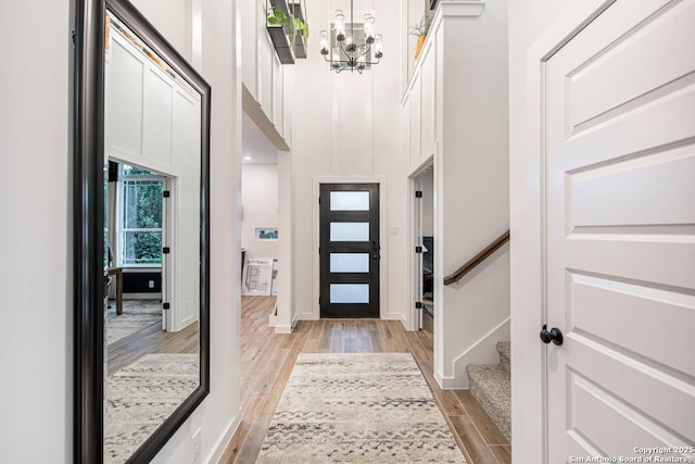 foyer featuring an inviting chandelier, a towering ceiling, baseboards, stairway, and light wood finished floors