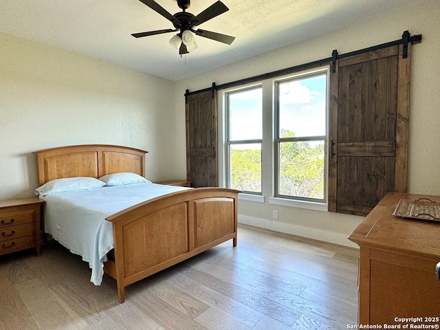 120 Sam Houston, Kerrville, TX 78028 - bedroom featuring a barn door, light wood-style flooring, baseboards, and ceiling fan