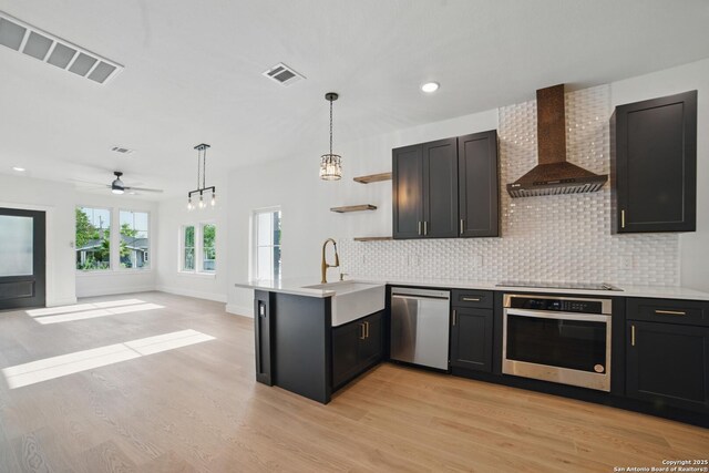 kitchen with open shelves, a peninsula, wall chimney exhaust hood, a sink, and appliances with stainless steel finishes