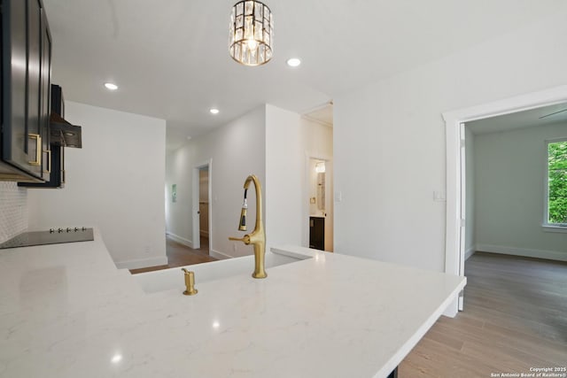 kitchen featuring stovetop, decorative light fixtures, a sink, light stone counters, and light wood finished floors