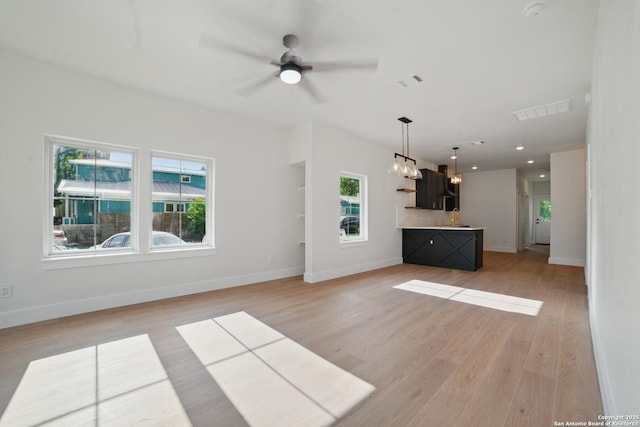 unfurnished living room with ceiling fan with notable chandelier, light wood finished floors, and visible vents