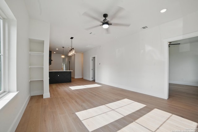 unfurnished living room with a ceiling fan, baseboards, visible vents, and light wood-style flooring