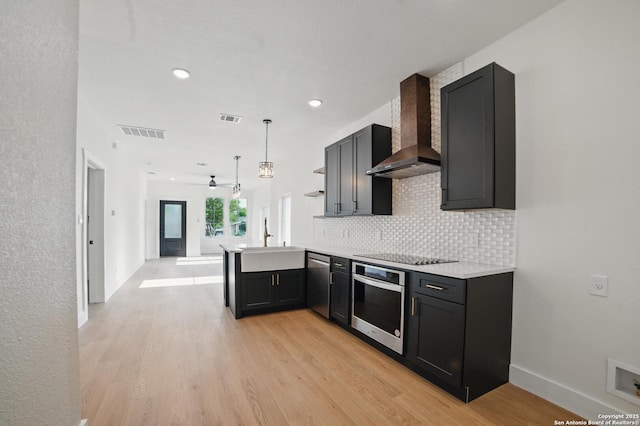 kitchen with visible vents, wall chimney range hood, a sink, light wood-style flooring, and appliances with stainless steel finishes