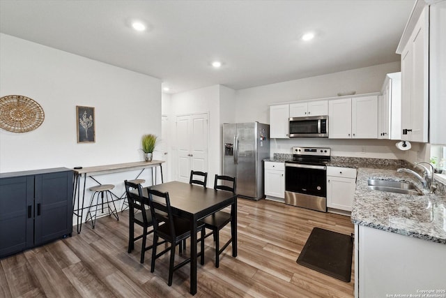 kitchen featuring a sink, light stone counters, light wood finished floors, stainless steel appliances, and white cabinetry