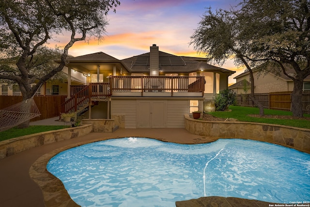 back of property at dusk with a wooden deck, a fenced backyard, a chimney, stairs, and roof mounted solar panels